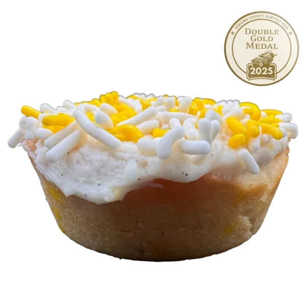 Lemon sugar cookie with yellow frosting, lemon zest, vanilla bean specks, and multicolored sprinkles on top.