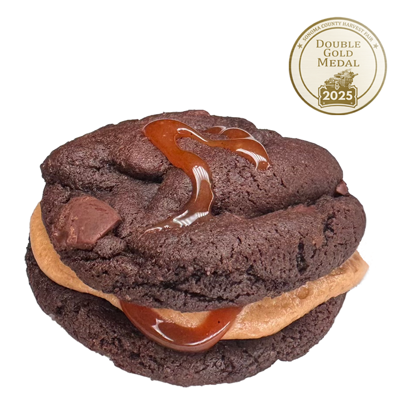 Chocolate Cookie Sandwich featuring chocolate chunks, filled with whiskey buttercream and drizzled with salted caramel.